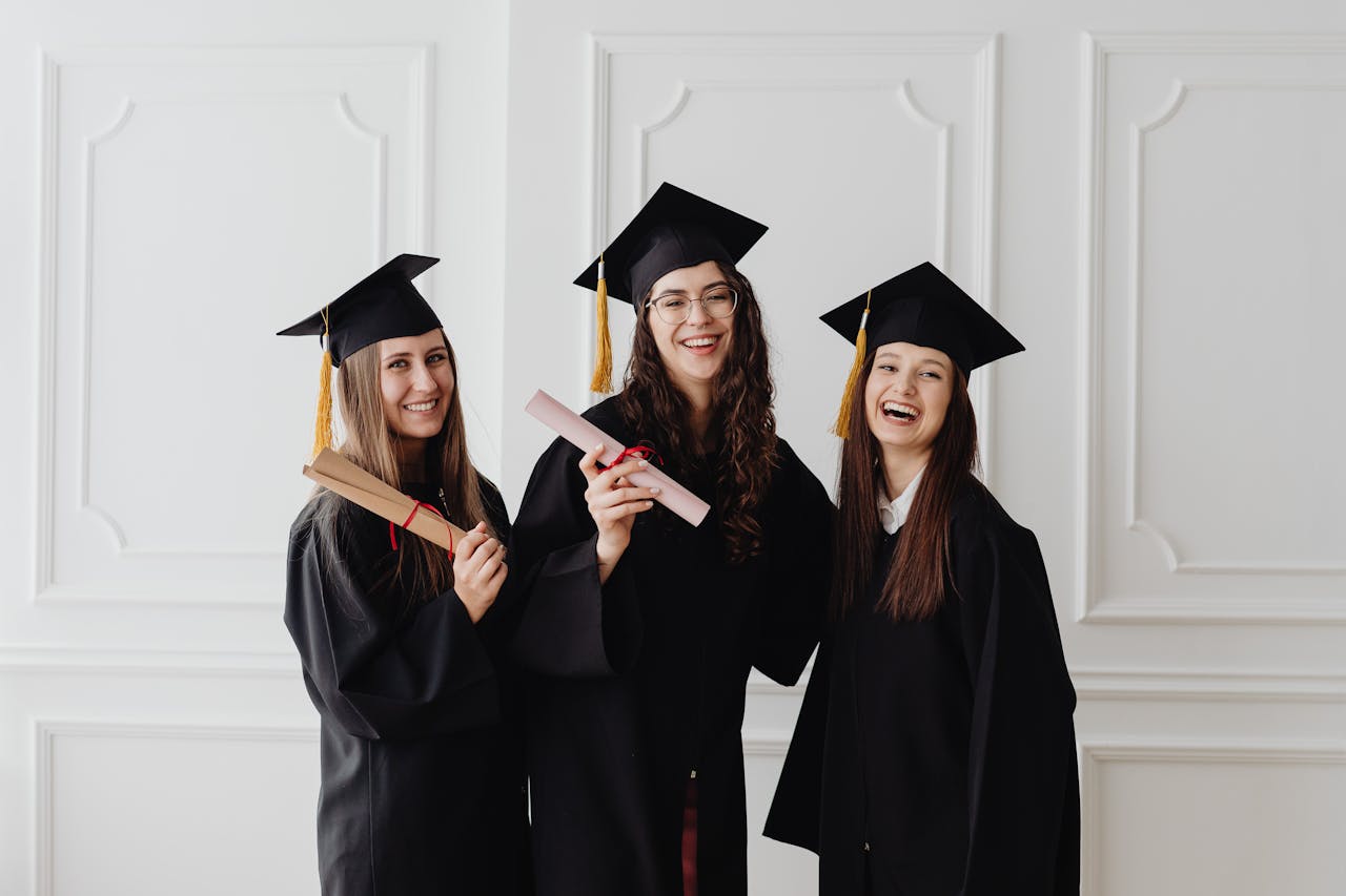 services-01 Three happy female graduates in caps and gowns holding diplomas and celebrating their achievement.